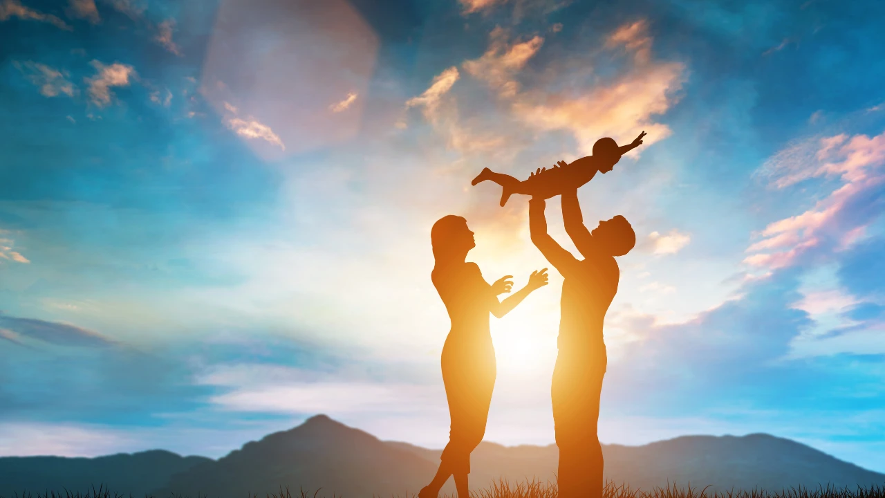2 parents face au soleil : le père porte son enfant dont celui-ci est en position "superman". Cela représente des liens familiaux forts