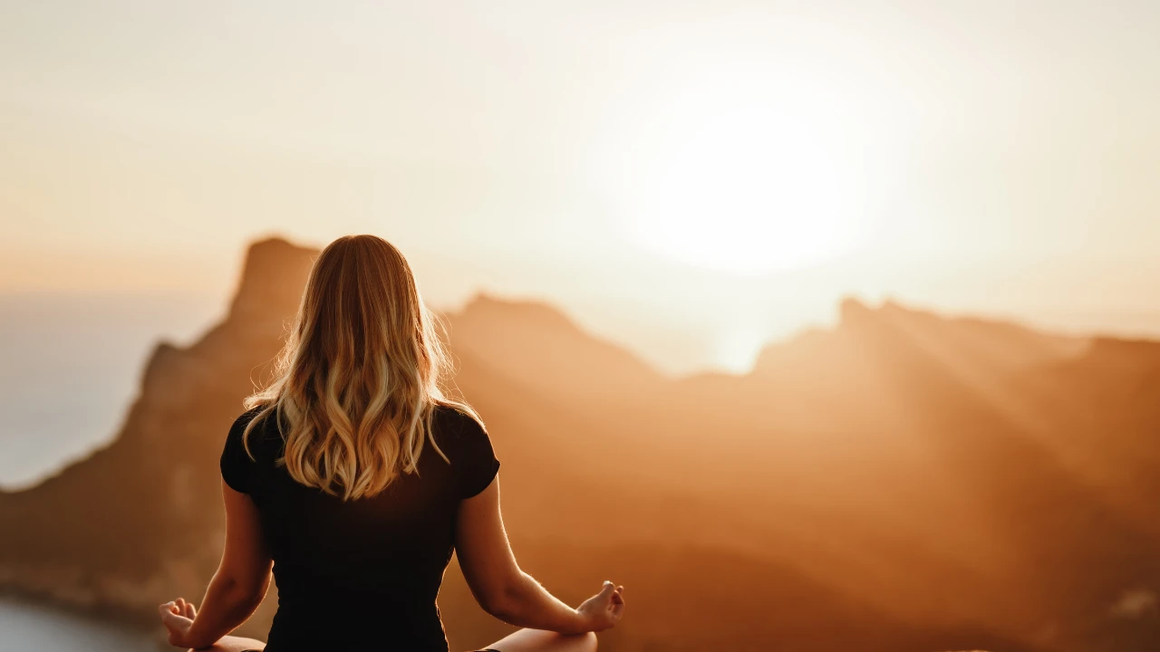 Femme en train de méditer devant un magnifique paysage et un soleil éclatant