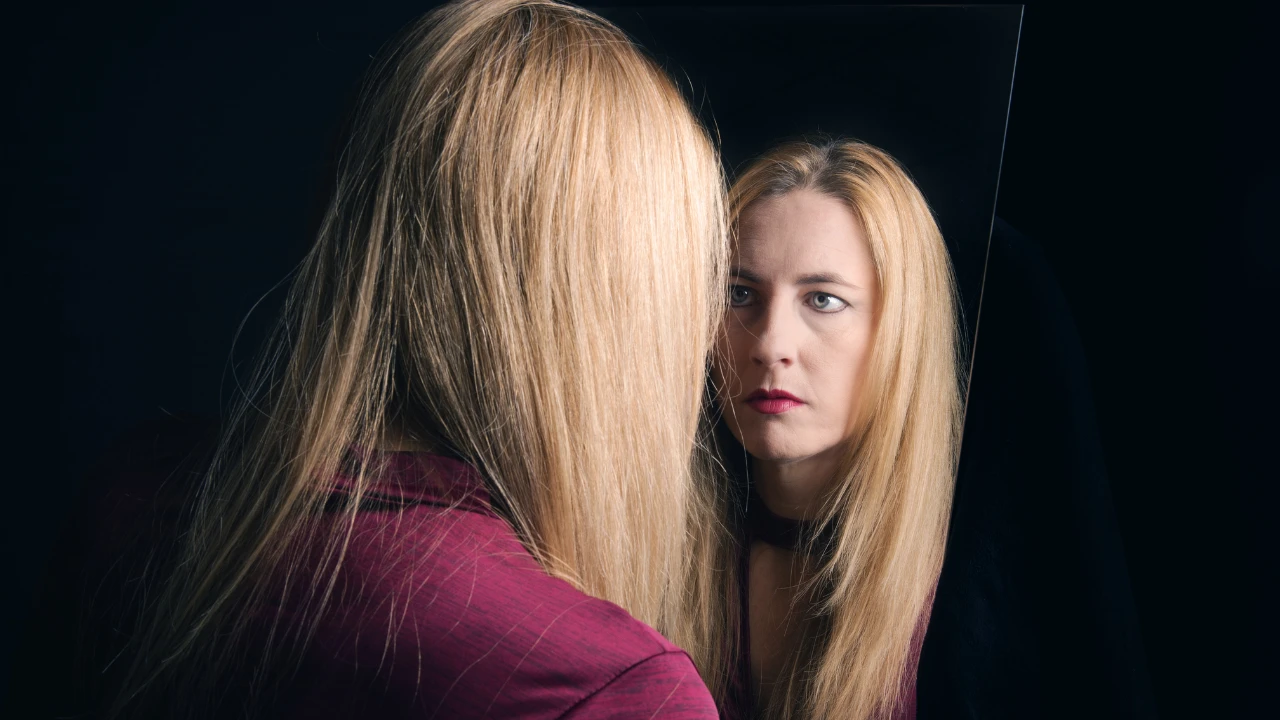 Femme blonde qui se regarde dans un miroir sur fond noir et qui représente l'observation de ses émotions