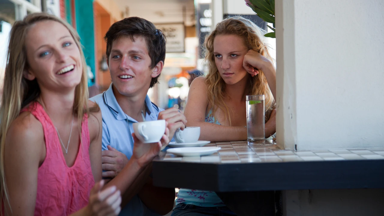 Couple qui discute dans un café avec une femme à côté au regard destructeur qui ressent de la jalousie