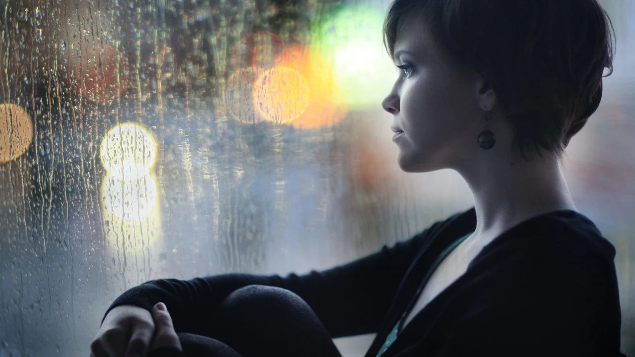 Femme triste qui regarde sa fenêtre avec des gouttes de pluie qui s'écoulent