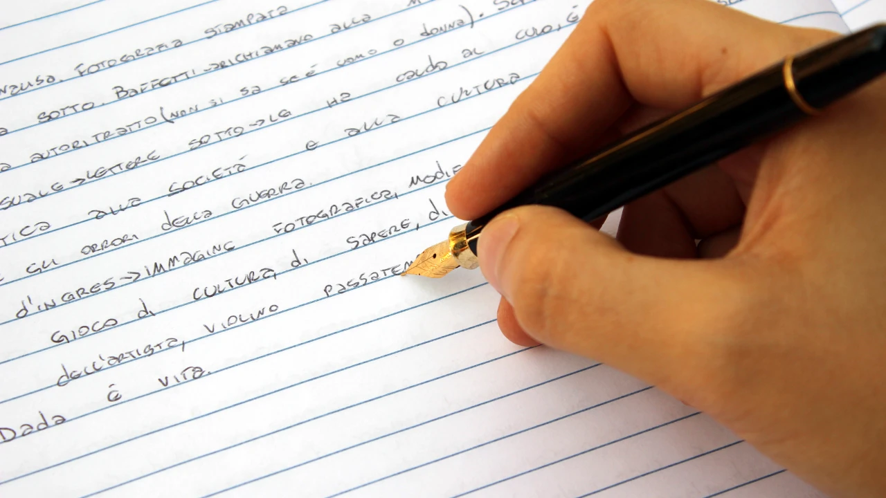 Stylo plume tenu à la main en train d'écrire sur du papier classique à ligne.